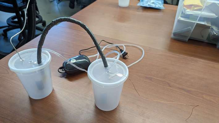 Two white plastic containers with lids in the shape of cups that are connected with a rope, which in turn is wrapped in electrical tape.